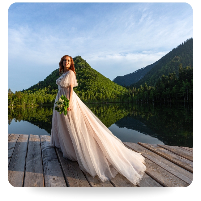 Bride on deck in front of lake and mountains looking off.